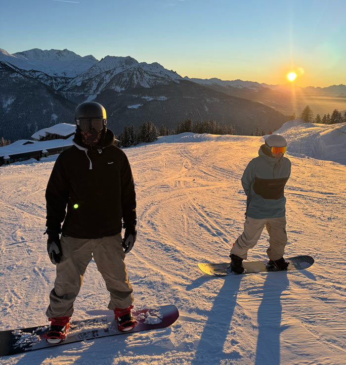 Twee snowboarders op de piste bij zonsondergang